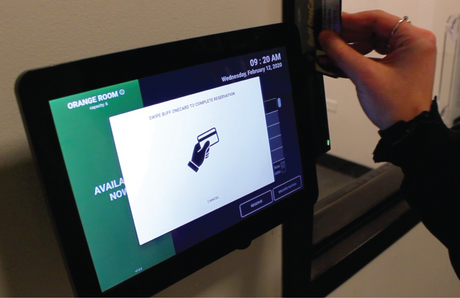 Swiping an ID card on the side of a wall-mounted room scheduling display